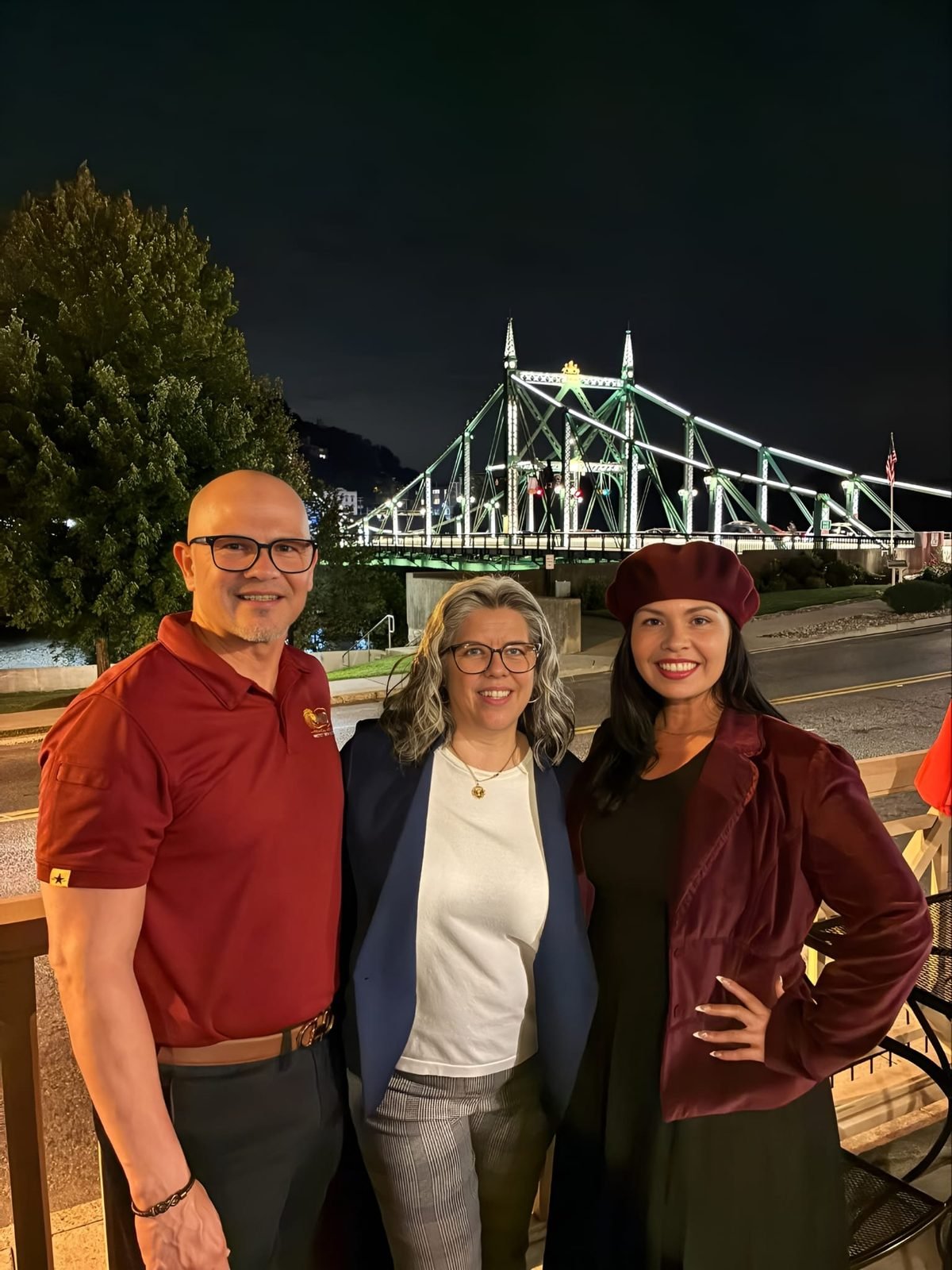 Tres asistentes posando juntos con el puente iluminado de fondo