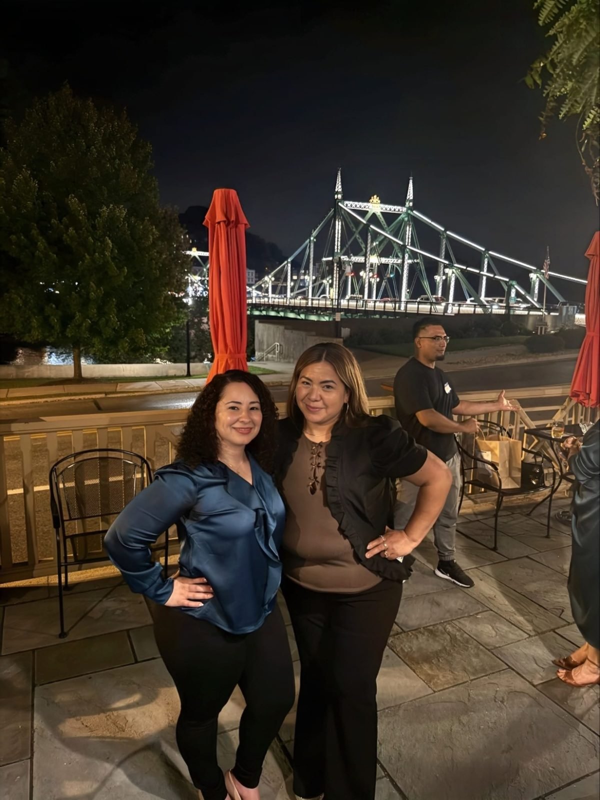 Dos emprendedoras posando en la terraza con el puente iluminado de fondo